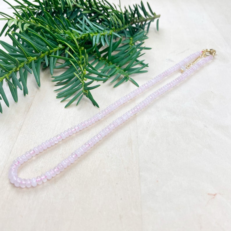 May include: A delicate pink beaded necklace with a gold clasp. The necklace is made of small, round beads and is approximately 18 inches long.