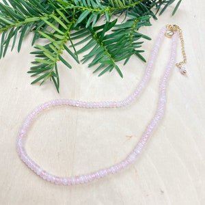 May include: A delicate pink beaded necklace with a gold clasp and extender chain. The necklace is made of small, round beads and is perfect for layering.
