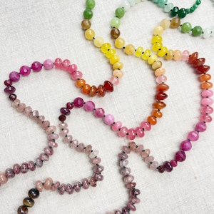May include: A collection of beaded necklaces in various colors, including green, yellow, orange, and pink. The necklaces are made of small, round beads strung together. The beads have a polished finish and are arranged in a gradient pattern.