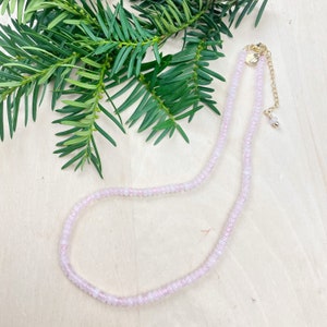 May include: A delicate pink beaded necklace with a gold clasp and extender chain. The necklace is made of small, round beads and has a subtle shimmer.