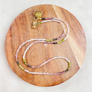 May include: A multi-strand necklace with pink, green, and black beads on a wooden surface.