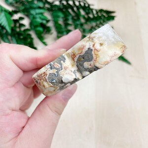 K&ouml;nnte beinhalten: Ein wei&szlig;er, brauner und grauer Achat-Stein mit einer einzigartigen, organischen Form. Der Stein hat eine glatte, polierte Oberfl&auml;che und ist perfekt f&uuml;r die Verwendung in der Kristallheilung oder als Dekorationsst&uuml;ck.