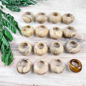 May include: A collection of 15 smooth, round, beige and brown stone rings with a hole in the center. One ring is a darker brown color with a glossy finish.