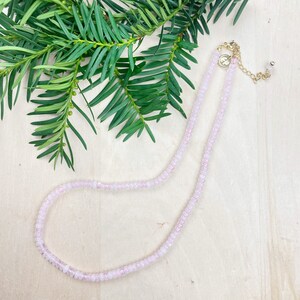 May include: A delicate pink beaded necklace with a gold clasp. The necklace is made of small, round beads and is perfect for layering.
