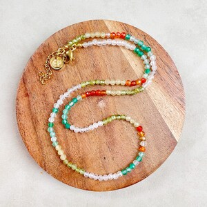 May include: A multi-colored beaded necklace with green, white, yellow, orange, and red beads. The necklace is on a wooden surface.