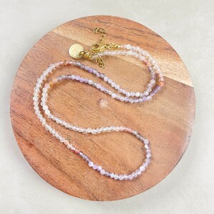 May include: A delicate layered necklace with small, clear, pink, and purple beads. The necklace has a gold clasp and a small gold charm.