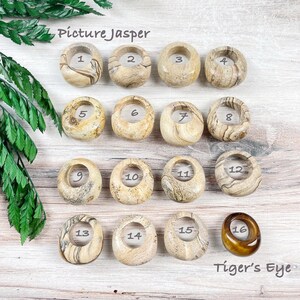 May include: A collection of 16 polished gemstone rings, numbered 1 through 16. The first 15 rings are made of picture jasper, a variety of jasper with a distinctive banded pattern. The last ring is made of tiger's eye, a chatoyant gemstone with a golden brown color.