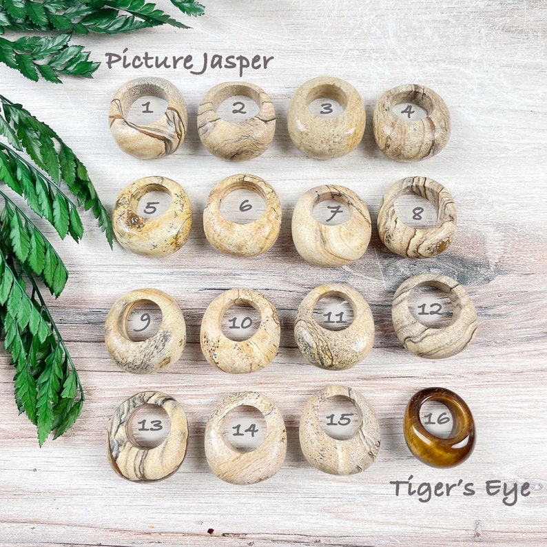 May include: A collection of 16 polished gemstone rings, numbered 1 through 16. The first 15 rings are made of picture jasper, a variety of jasper with a distinctive banded pattern. The last ring is made of tiger's eye, a chatoyant gemstone with a golden brown color.