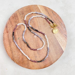 May include: A multi-colored beaded necklace with a gold clasp and a small gold charm with the letters "EP" on a wooden surface.