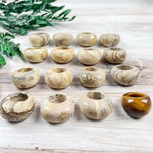 May include: A collection of 15 smooth, round, beige and brown stone rings with a tiger eye stone ring in the center.