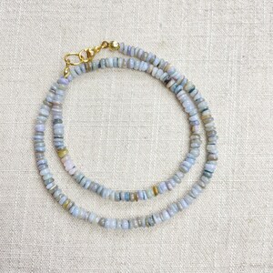 May include: A delicate necklace featuring small, round, light blue and grey beads. The beads are strung together, forming a double strand. The necklace is secured with a gold-coloured clasp.