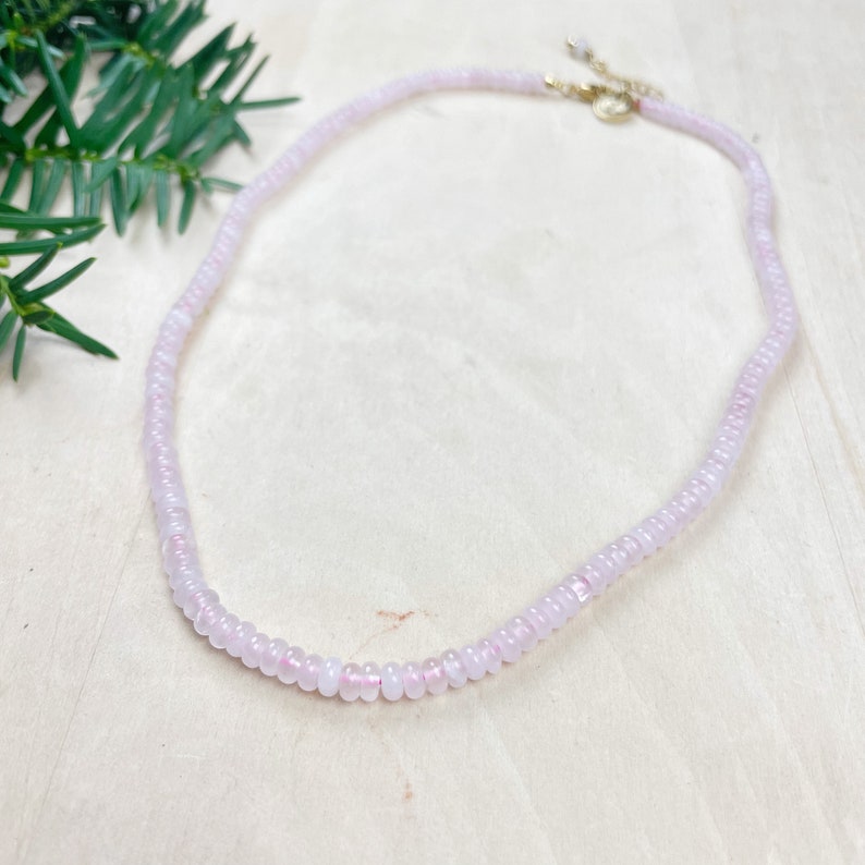 May include: A delicate pink beaded necklace with a gold clasp. The necklace is made of small, round beads and is perfect for layering with other necklaces.