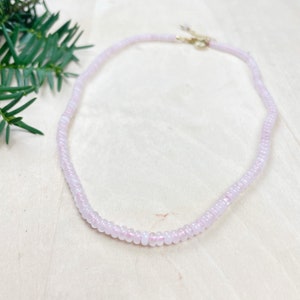May include: A delicate pink beaded necklace with a gold clasp. The necklace is made of small, round beads that are strung together to create a simple and elegant design.