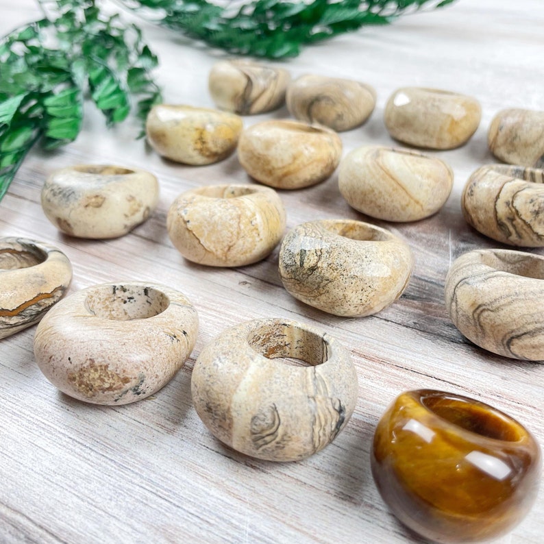 May include: A collection of beige and brown banded agate rings with a single tiger's eye ring.