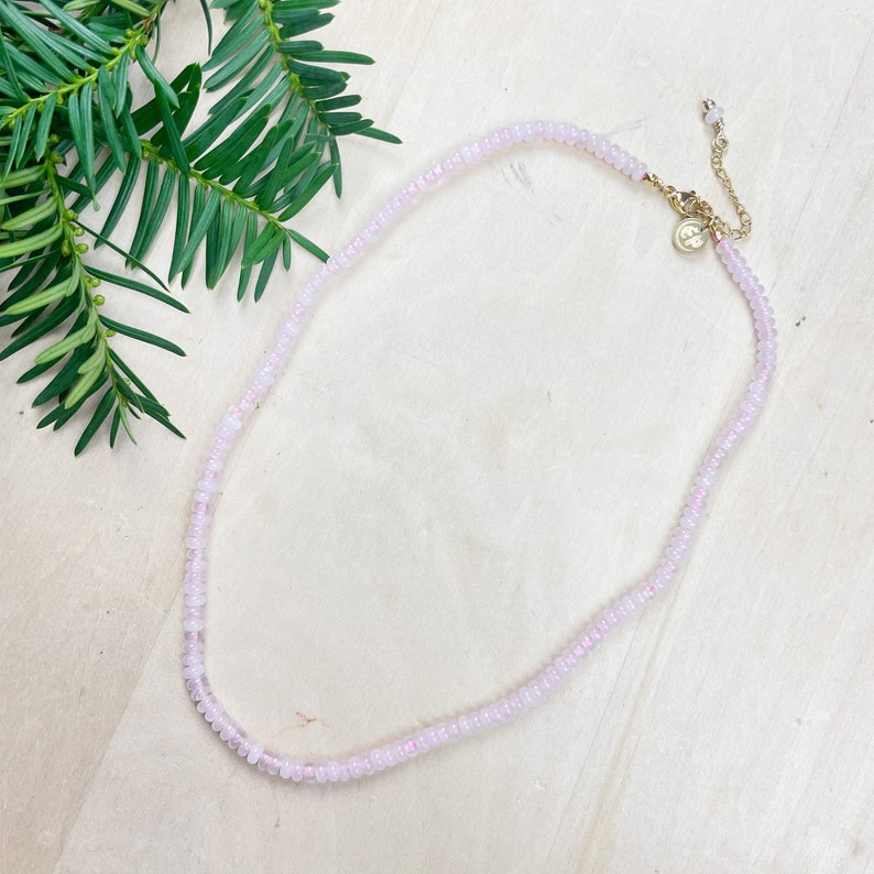 May include: A delicate pink beaded necklace with a gold clasp and extender chain. The necklace is made of small, round beads and is perfect for layering.