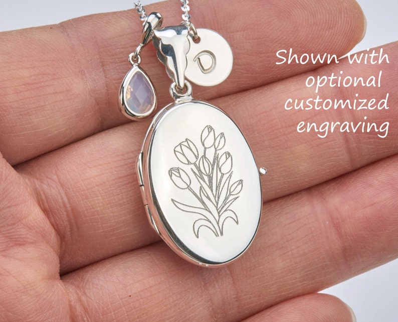 May include: Silver locket necklace with a tulip engraving. The locket has a small, clear teardrop charm and a round charm with the letter "D" engraved on it. Shown with optional customized engraving.