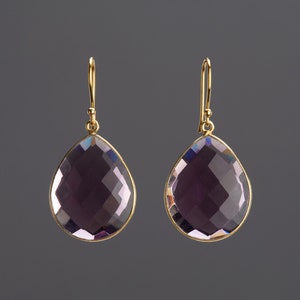 May include: A pair of gold earrings with a teardrop-shaped amethyst gemstone.