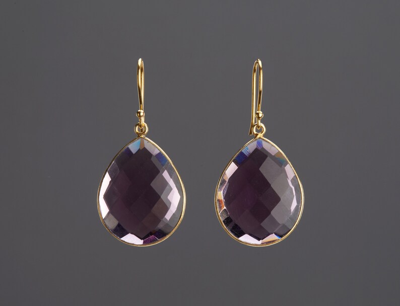 May include: A pair of gold earrings with a teardrop-shaped amethyst gemstone.