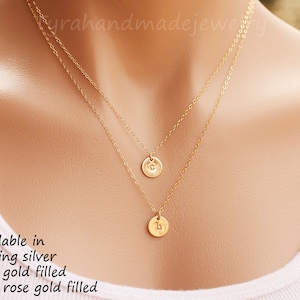 Puede incluir: Un collar de oro de dos capas con dos pequeños colgantes redondos. Los colgantes tienen las letras "C" y "B" grabadas. Disponible en plata de ley, oro de 14 quilates relleno y oro rosa de 14 quilates relleno.