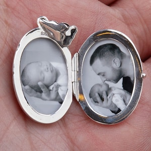 May include: Silver oval locket with two photos inside. The locket is open and shows a photo of a baby sleeping in a hand and a photo of a man kissing a baby on the forehead.