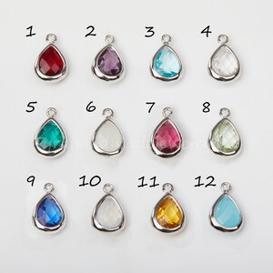 May include: Twelve teardrop-shaped glass charms with silver settings. The charms are numbered 1 through 12 and come in a variety of colors, including red, purple, blue, green, white, and yellow.
