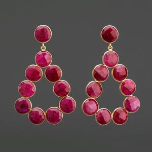 Puede incluir: Un par de pendientes colgantes con forma de lágrima. Los pendientes están hechos de oro y presentan múltiples piedras redondas, facetadas, de color rojo rubí.