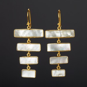 May include: A pair of gold earrings with five white rectangular mother-of-pearl stones hanging from each earring.