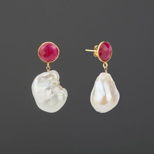 May include: A pair of drop earrings featuring round, faceted, deep pink gemstones set in gold, each suspending a large, irregular, white baroque pearl. The earrings utilize a post-back closure mechanism, showcasing the contrast between the vibrant pink stones and the lustrous, organic shapes of the white pearls.