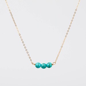 May include: A delicate gold-colored necklace featuring three turquoise-colored beads. The beads are evenly spaced along the necklace's chain. The necklace is displayed against a plain white background.