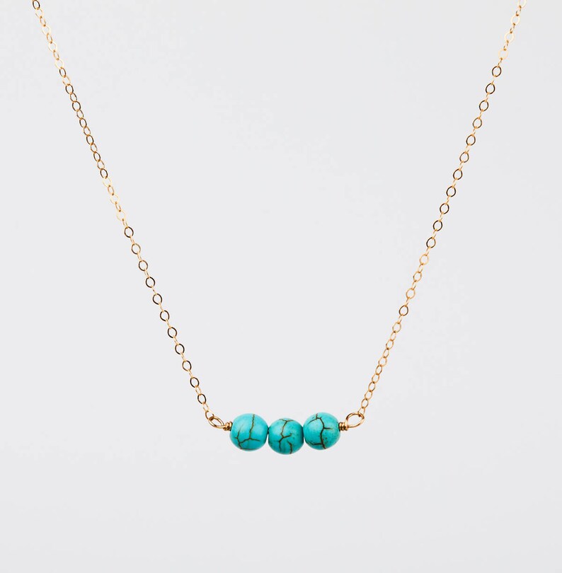 May include: A delicate gold-colored necklace featuring three turquoise-colored beads. The beads are evenly spaced along the necklace's chain. The necklace is displayed against a plain white background.