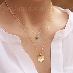 May include: A gold layered necklace with a turquoise stone pendant and a hammered gold disc pendant.