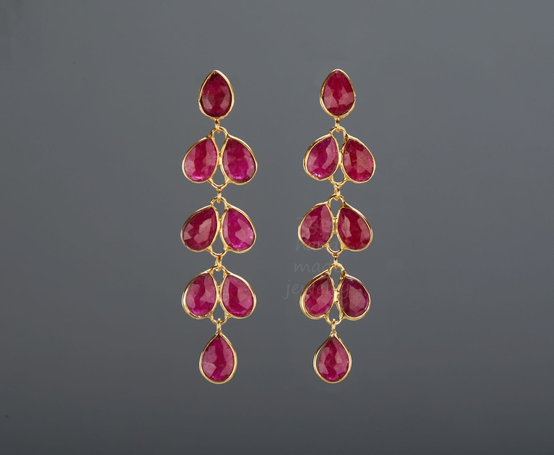 May include: A pair of long, dangling earrings featuring multiple teardrop-shaped ruby red stones. The earrings are crafted from gold and have a delicate, feminine design.