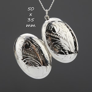 Könnte beinhalten: Silberne Halskette mit einem ovalen Anhänger und einem gravierten Blumenmuster. Der Anhänger ist 50 x 35 mm groß.