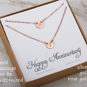 May include: A gift box containing a rose gold necklace with two initial charms. The box features a card that reads "Happy Anniversary" and "Handmade in USA". The box also has the words "silver", "gold", and "rose gold" printed on it.
