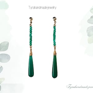 Könnte beinhalten: Ein Paar lange, grüne Edelstein-Ohrhänger mit goldenen Akzenten. Die Ohrringe bestehen aus kleinen, runden grünen Perlen und einem tropfenförmigen grünen Edelstein am unteren Ende.