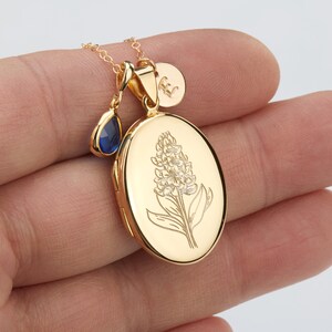 May include: A gold locket necklace with a floral design and a blue teardrop charm. The locket is oval shaped and has a delicate chain.