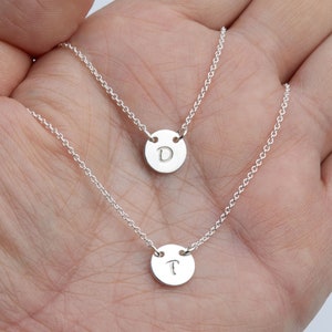 May include: Two silver necklaces with initial pendants. The top necklace has a pendant with the letter "D" and the bottom necklace has a pendant with the letter "T".