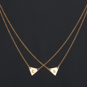 May include: A gold chain necklace with two triangle pendants, one with the letter "C" and the other with the letter "S".