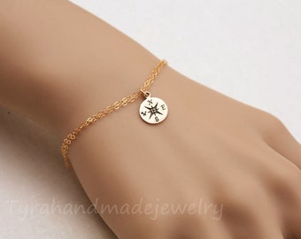 May include: A gold chain bracelet with a compass charm. The compass charm has the directions N, E, S, and W engraved on it.