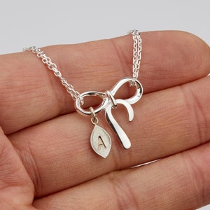 May include: Silver necklace with a bow charm and a leaf pendant with the letter A engraved on it.