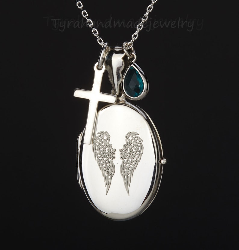May include: Silver locket necklace with a cross charm and a teardrop-shaped blue gemstone. The locket features an engraved design of angel wings.