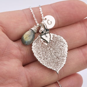 Puede incluir: Collar de plata con un delicado colgante de hoja de plata, una peque&ntilde;a piedra de labradorita en forma de l&aacute;grima y un dije de plata con la letra 'C'.