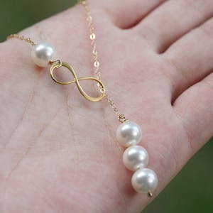 May include: A gold infinity symbol pendant necklace with a single pearl at the top and three pearls dangling from the bottom.