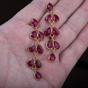 May include: A pair of long, dangling earrings with multiple teardrop-shaped ruby red stones set in gold.