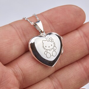 May include: Silver heart-shaped locket necklace with a delicate chain. The locket features an engraved image of Hello Kitty.