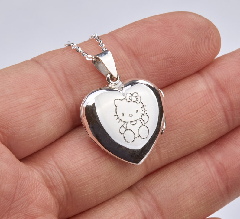 May include: Silver heart-shaped locket necklace with a delicate chain. The locket features an engraved image of Hello Kitty.