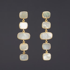 May include: A pair of gold earrings with five white rectangular mother-of-pearl stones hanging from each earring.