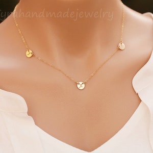 May include: A gold chain necklace with three small round pendants, each with a different letter engraved on it.