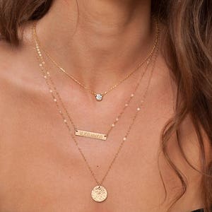 May include: A layered gold necklace with a small round pendant, a rectangular bar pendant with roman numerals, and a hammered round pendant.
