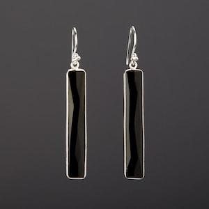Könnte beinhalten: Ein Paar silberne Ohrringe mit schwarzen rechteckigen Edelsteinen.